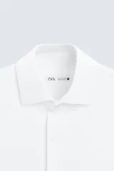 Camisa color beige de corte slim fit, confeccionada en tejido elástico que minimiza las arrugas. Tiene cuello italiano abierto, manga larga con puños abotonados y cierre frontal con botones.