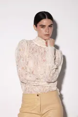 Blusa de encaje color manteca, con cuello alto estilo pañuelo que se ata en la parte posterior y mangas abullonadas en los hombros.