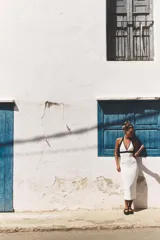 Vestido midi blanco de tejido elástico, con cuello halter, escote pico, falsos bolsillos de vivo con botón y acabados a contraste en negro.