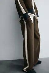 Pantalón jogger color verde oliva, corte relaxed fit, con cintura elástica ajustable con cordón, bolsillos laterales y detalle de bolsillo de vivo en la espalda. Presenta una banda lateral color crema a contraste.