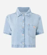 Camisa cropped de jeans celeste con cuello clásico, mangas cortas, cierre frontal con botones y bolsillo en el pecho.