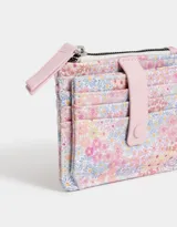 Billetera pequeña de cuerina estampada con flores de colores. Tiene cierre superior con tirador rosa, lazo con broche a presión y compartimentos para tarjetas.