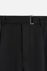 Pantalón negro de corte amplio, con pliegues frontales, bolsillos laterales y traseros de ojal. Incluye cinturón de la misma tela con hebilla metálica.
