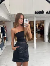 Pollera corta negra de ecocuero, con cortes y detalles de bolsillos grandes.