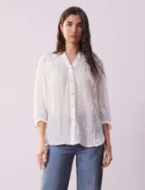 Blusa blanca de gasa marca Figueroa & Flower, con cuello a la base, escote en V y abertura central con botones. Presenta detalles de crochet en hombros y espalda, mangas 3/4 amplias con puño y botón.
