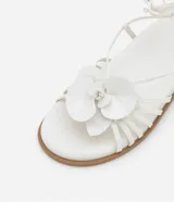 Sandalias planas blancas de cuero sintético, con tiras finas, puntera redonda, lazo para atar al tobillo y maxi flor aplicada en la capellada.