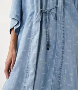 Kimono de lyocell (tejido tipo jean) color celeste claro con estampado repetitivo de pequeños peces blancos. Diseño de manga corta ancha y abertura frontal que se ajusta con un lazo fino en la cintura.