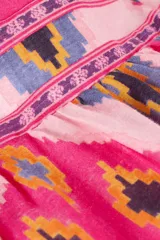 Vestido largo strapless con estampado geométrico en tonos rosados, fucsias, morados y negros. Tiene lazo para atar alrededor del cuello y detalle retorcido en el frente y en la espalda.