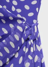 Vestido corto de poliéster, color azul con estampado de lunares blancos. Presenta cuello pico cruzado, tirantes anchos y diseño evasé con cierre lazo cruzado en la cintura.