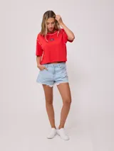 Remera gris de algodón con corte cropped y calce holgado. Tiene cuello redondo y mangas cortas con costuras reforzadas en color coral. Presenta un pequeño logo de la marca Rusty en el pecho.