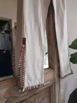 Pantalón de jean blanco con corte acampanado, cintura alta, detalles trenzados y aplicaciones de cuero en la parte inferior.