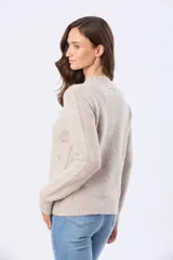 Buzo tejido de abrigo color beige, con cuello redondo y mangas largas. Presenta un delicado diseño bordado en el frente con pequeños motivos en tonos pastel.