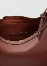 Cartera tipo riñonera color marrón, con efecto piel y forma de media luna. Tiene cierre de cremallera, forro interior y asa bandolera ajustable con hebillas.