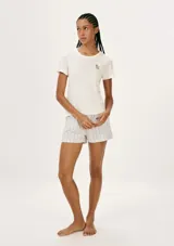 Conjunto de pijama femenino compuesto por una remera de manga corta color blanco hueso con un pequeño bordado de flor en el pecho, y un short de tiro medio con estampado de rayas verticales finas en tonos beige y rosado.