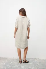 Vestido tipo camisa color crudo, de corte recto, con cuello camisero, mangas 3/4 con trabillas y cierre frontal con botones.