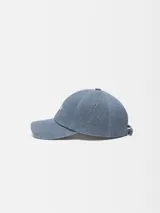 Gorra de denim azul con visera corta y logo metálico plateado en el frente.