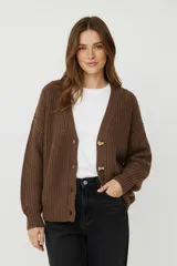 Cardigan de punto acrílico color crema, con cuello en V, manga larga y botones frontales. Presenta un tejido acanalado grueso y un calce holgado.