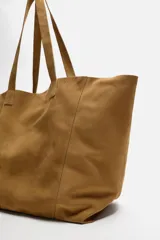 Bolso tipo shopper color marrón claro, fabricado en piel serraje. Cuenta con dos asas de mano y un bolsillo interior con cierre de cremallera.