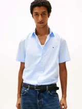 Camisa de manga corta Tommy Hilfiger confeccionada en popelín elástico de algodón BCI color celeste, con cuello abotonado, cierre con botones y logo bordado en el pecho.