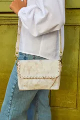 Cartera bandolera de cuero color blanco envejecido con pespuntes marrones. Tiene correa larga regulable y herrajes metálicos color bronce.