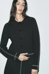 Chaqueta corta negra de punto con cuello solapa, manga larga y cierre frontal con botones.