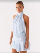 Vestido corto celeste con escote halter, espalda descubierta, falda con volados y pliegues en la cintura.