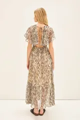 Vestido largo de viscosa jacquard con estampado de cebra en tonos marrón y negro, con detalles de lurex dorado. Presenta escote en V cruzado, elástico en la cintura y mangas cortas con volados.