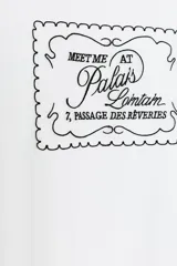 Camiseta blanca de algodón con cuello redondo y mangas cortas. Estampado frontal con texto "Meet me at Palais Lomtam, 7, Passage des Rêveries" enmarcado en un diseño ondulado.