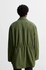 Parka verde militar de tejido técnico ligero, corte relaxed fit, cuello solapa y manga larga. Tiene cuatro bolsillos de plastrón con solapa en el delantero, cintura ajustable en el interior y cierre frontal con cremallera oculta por solapa con botones a presión.
