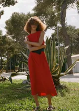 Vestido midi rojo sin mangas, con cuello redondo y corte evasé. Presenta pinzas en la cintura y cierre de cremallera y botón en la parte posterior.