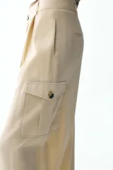 Pantalón color beige de tiro alto con bolsillos delanteros, bolsillos de plastrón con solapa laterales y falsos bolsillos de vivo en la espalda. Bajo acabado con trabilla y botón. Cierre frontal con cremallera y botón.