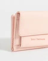 Billetera color rosa claro de cuerina engomada con solapa y tag en relieve con la frase "Tres Charmant". Tiene compartimentos para tarjetas y billetes.
