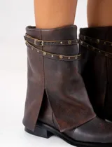 Bota corta de cuero color marrón con suela de goma negra, taco de madera de 3cm y caña de 25cm. Presenta una correa con hebilla y tachas pequeñas alrededor del tobillo.