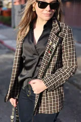 Blazer de tweed con estampado pata de gallo en tonos marrón y beige, con solapas con detalle de pines decorativos.