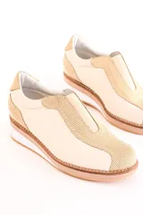Zapatillas deportivas color beige con detalles en dorado, sin cordones y suela de goma.