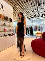 Vestido negro con escote strapless, corte ajustado al cuerpo y falda midi con abertura lateral y sobrefalda de tul transparente.