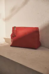 Neceser tipo sobre de cuero color rojo con cierre superior y detalle de borla de flecos en el tirador del cierre.