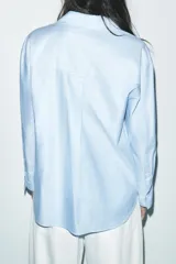 Camisa celeste de corte clásico, con cuello solapa, manga larga, bajo asimétrico y cierre frontal con botones.