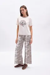 Pantalón de tiro alto, corte ancho y largo, con estampado de piel de serpiente en tonos beige y marrón. Presenta costuras visibles en color marrón oscuro.