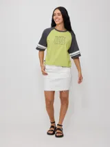 Remera bicolor Rusty con cuerpo verde lima y mangas ranglán grises con dos rayas blancas en los puños. Estampado frontal con el logo de la marca y el número 85.