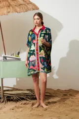 Túnica de viscosa color verde oscuro con estampado temático de playa y cócteles, cuello camisero con solapas en rojo y carmesí, y tapeta de botones a cuadros multicolores.
