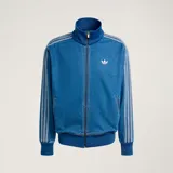 Campera deportiva Adidas Originals modelo Firebird, confeccionada en denim azul. Presenta cuello alto, cierre frontal, puños y cintura de tejido acanalado azul oscuro, y las tres franjas características de Adidas en las mangas en tono más claro. Incluye el logo del trébol bordado en blanco en el pecho.