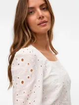 Blusa corta blanca con bordado calado, cuello cuadrado y mangas largas abullonadas con puños elásticos. Confeccionada en algodón.
