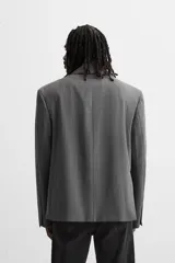 Blazer gris con raya diplomática, corte boxy, cuello con solapas de muesca, manga larga con puño abotonado, bolsillo de vivo en pecho, aberturas en espalda y cierre frontal con dos botones.