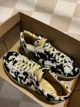 Zapatillas bajas con estampado animal print de vaca en blanco y negro, con cordones marrones y suela color caramelo.