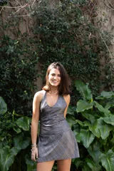 Vestido plateado con rayas horizontales negras, escote en V y breteles finos que se atan atrás del cuello. Corte en la cadera y falda con ruedo irregular y pico en lateral.