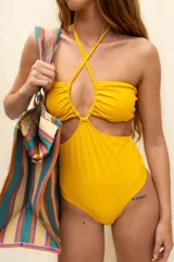 Traje de baño entero color amarillo mostaza, con diseño cut-out en el abdomen y escote fruncido. Presenta tiras finas que se cruzan en el escote y se atan en el cuello (halter).