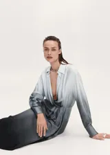 Vestido camisero midi con efecto tie-dye degradado de celeste a gris oscuro. Tiene cuello camisero, escote en V, mangas largas con puños abotonados, corte recto, tejido satinado y bajo asimétrico.