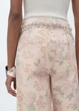 Pantalón de jean de corte wide leg con estampado floral en tonos pastel. Tiene tiro alto, cinco bolsillos, trabillas y cierre frontal con cremallera y botón.