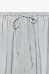 Pantalón de tiro medio color celeste confeccionado en hilatura con mezcla de lyocell. Tiene bolsillos laterales, pinzas en el delantero y pierna ancha. Cierre frontal con cremallera, botón y ganchos metálicos.